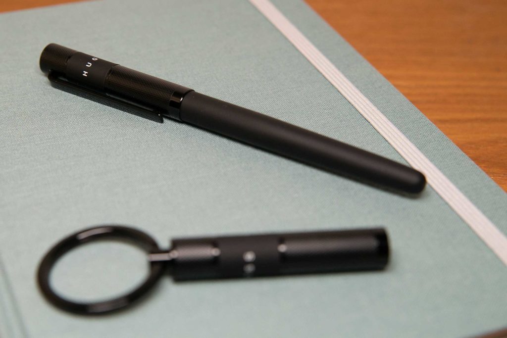 Der Hugo Boss Ribbon Black mit Schlüsselanhänger auf einem Notizbuch.